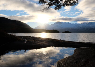 Fjord de Patagonie avec eau gelée au premier plan, un voilier au mouillage et des montagnes couvertes de neige et de glaciers en arrière plan.