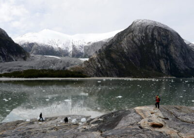 Trois personnes marchant sur les rives d'un fjord avec le glacier Pia en arrière plan.